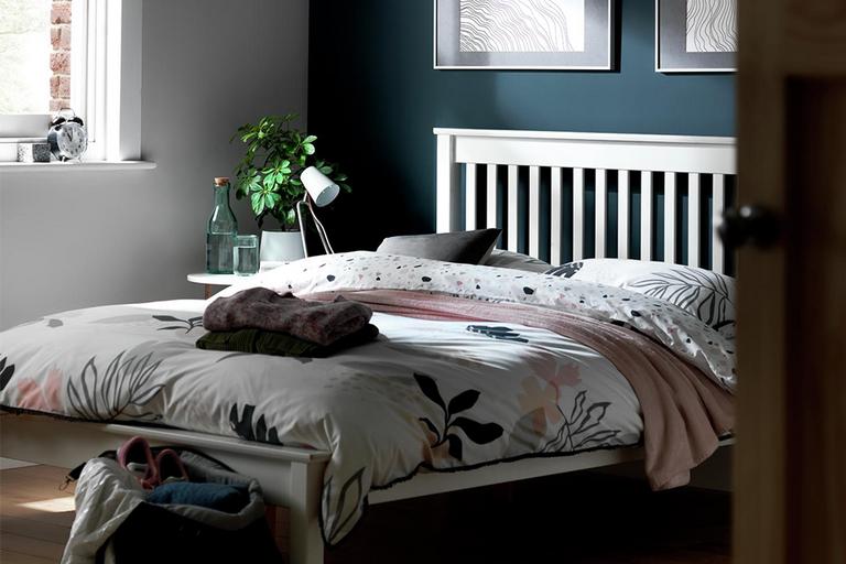 Dark blue bedroom with white bed frame and leaf print bedding.