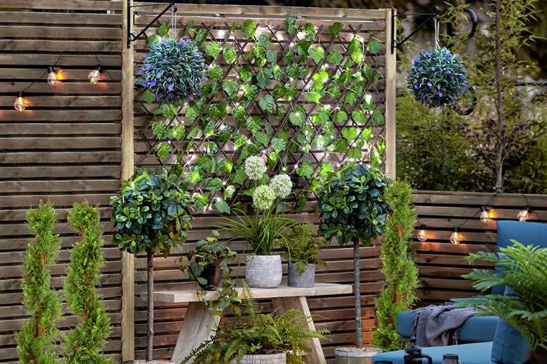 Image of a patio area with plants, outdoor seating and string lights.