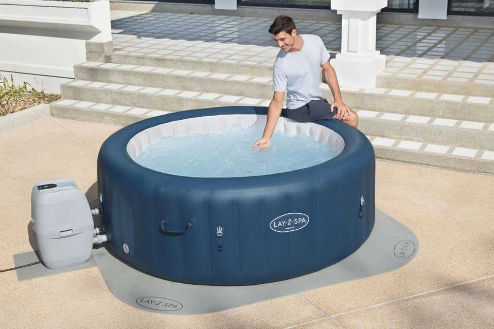 A man checking the water temperature of a hot tub, placed on top of a Lay-Z-Spa floor protector.