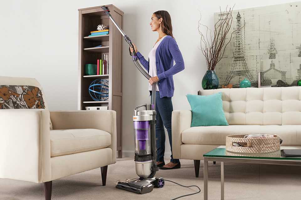 A woman cleaning the bookshelf with a Vax Air Stretch Max Pet corded upright vacuum cleaner.