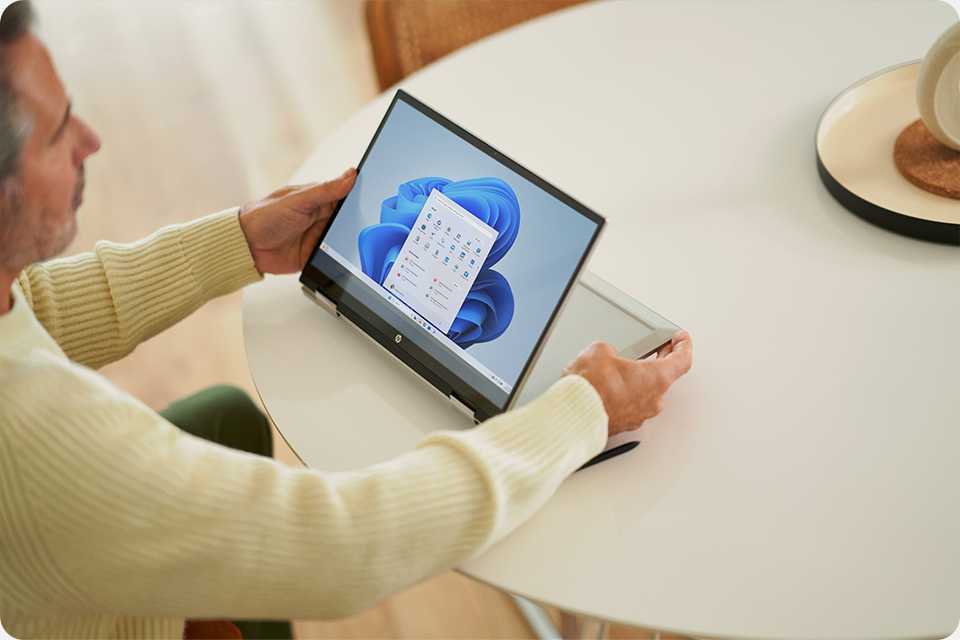 A person working on a silver Microsoft Windows 11 laptop on a table top.