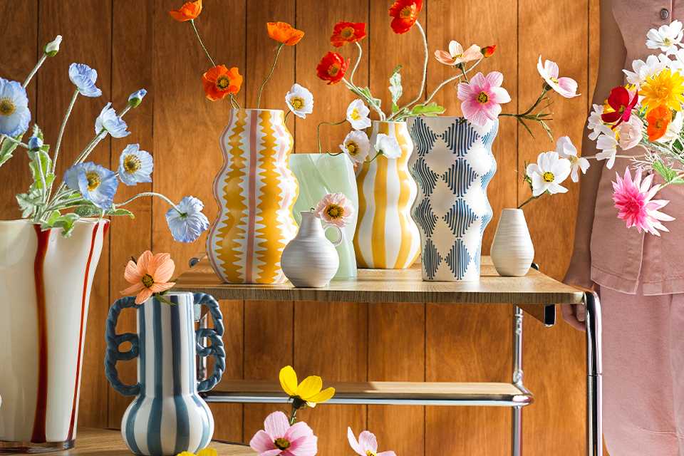 A person standing next to colourful vases with flowers in them.