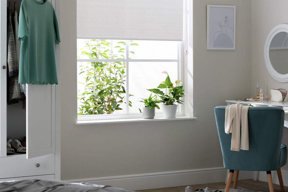 Bedroom with white roller blinds and dressing table.