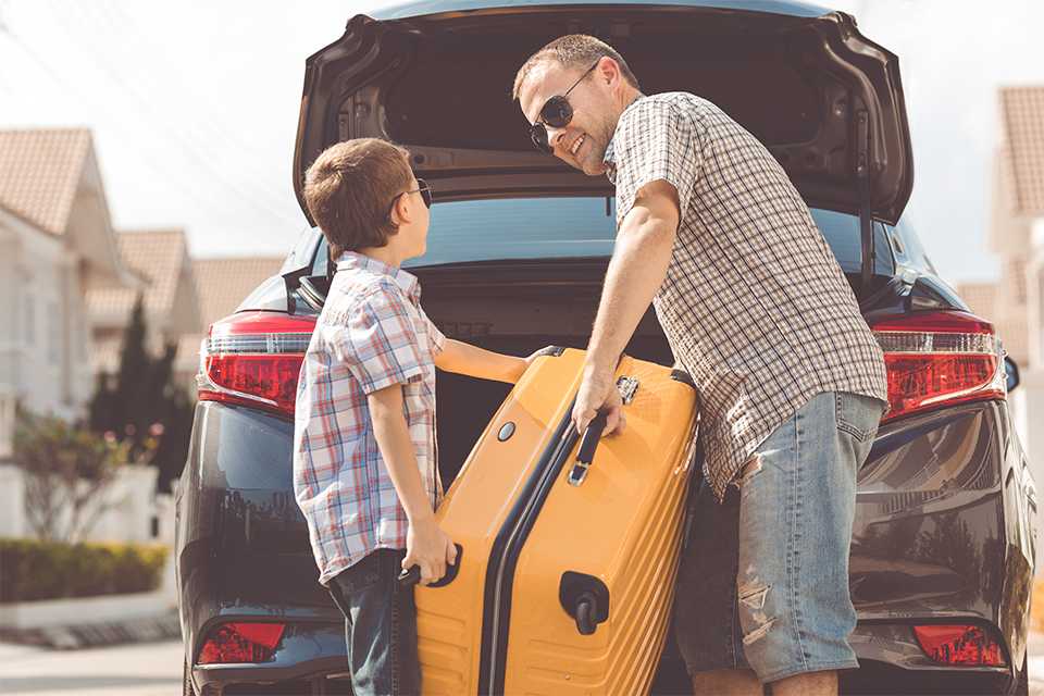 A father and son loading a yellow suitcase in the car.