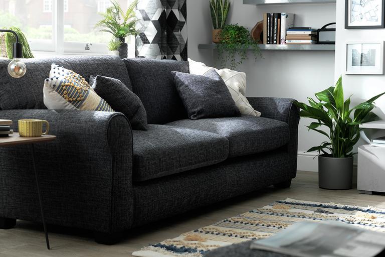 Grey fabric upholstered sofa in a grey and white lounge, with mustard accents and green houseplants.