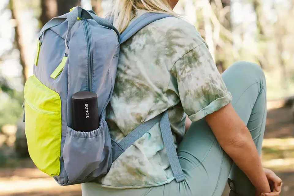 A portable small speaker in a bottle holder of a bag worn by a girl.