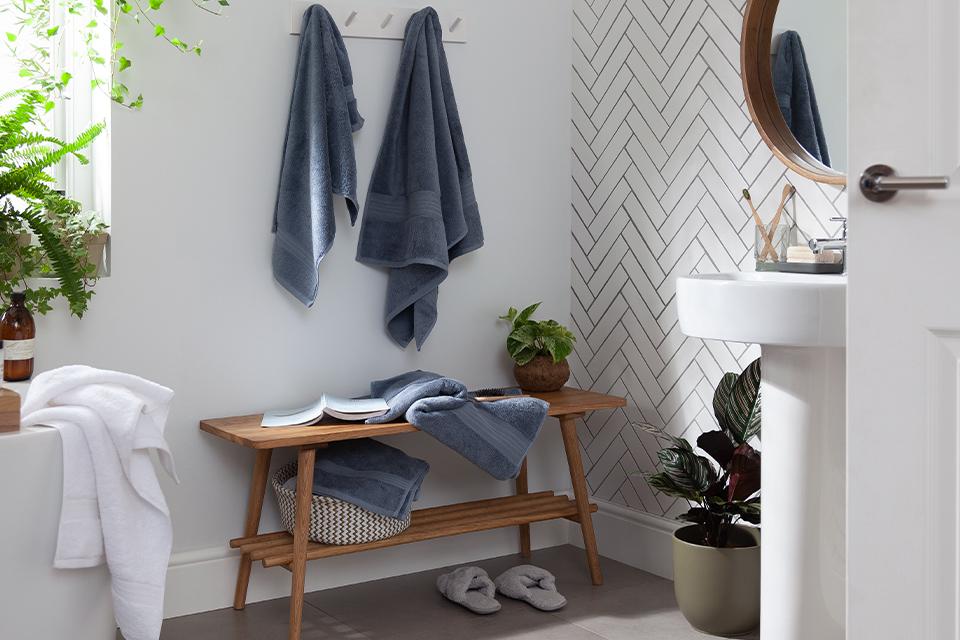 A white bathroom with a wooden bench and blue-grey towels.
