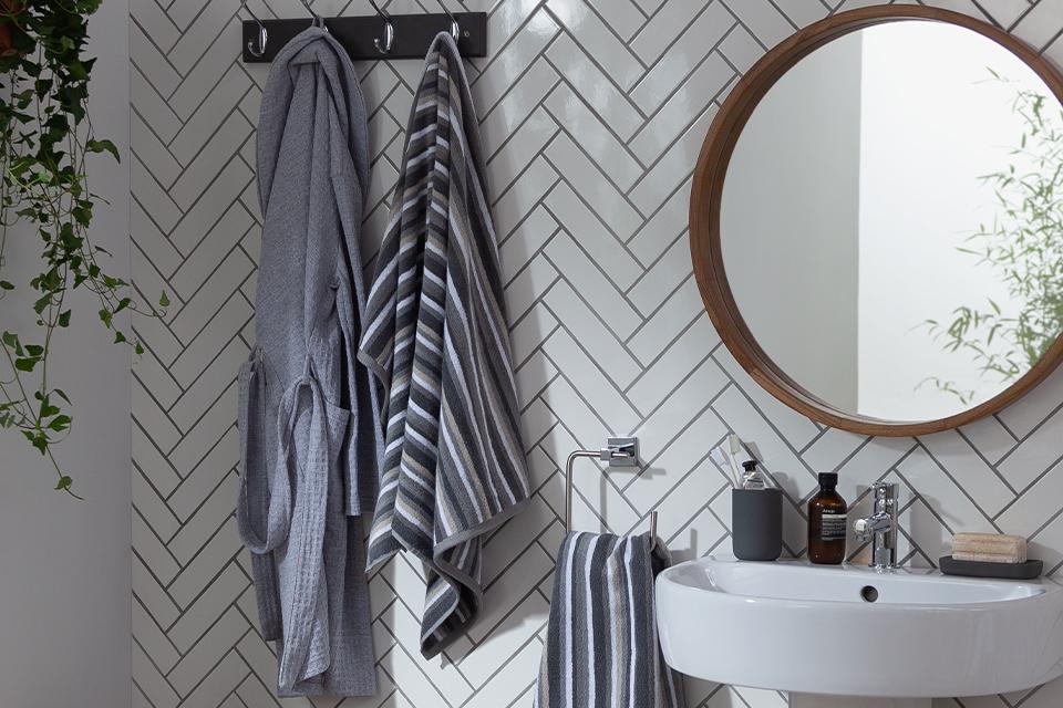 Grey striped towels and a grey bathrobe hung on a white tiled wall.
