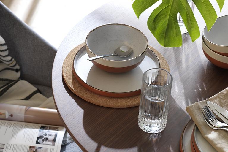 A round wooden table laid out for breakfast with white and ochre stoneware crockery.