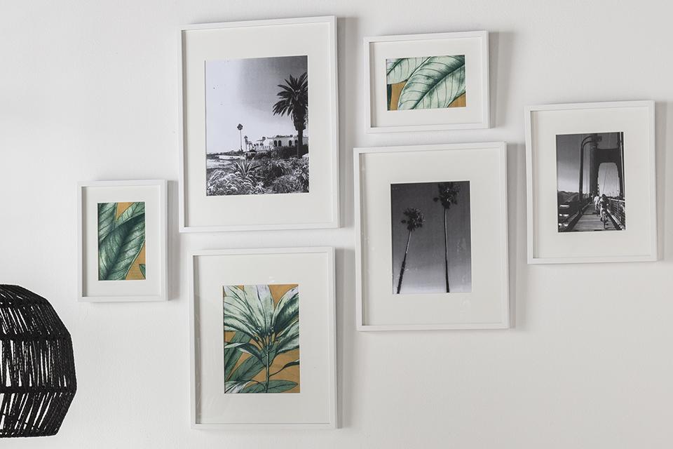 Six different sized art prints in white frames arranged together on a white wall.