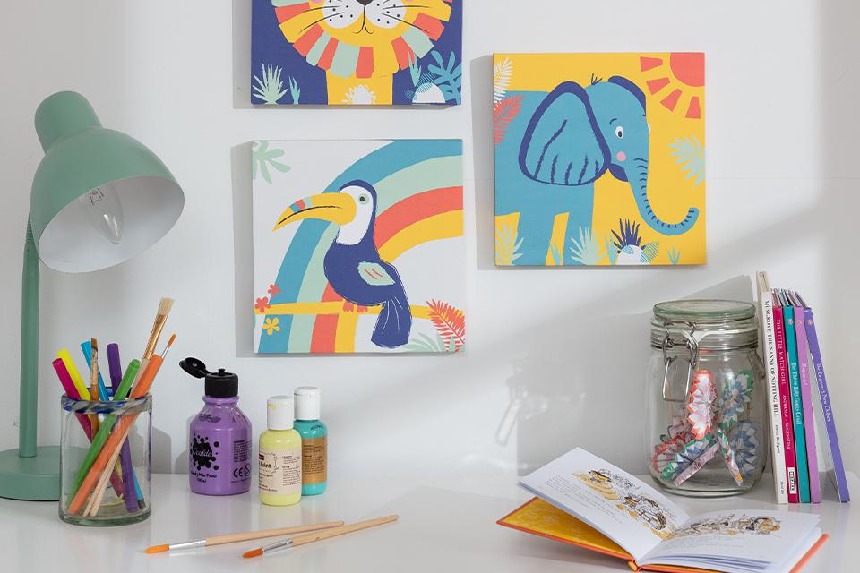 Brightly coloured kids' art prints arranged on a wall above a craft table.