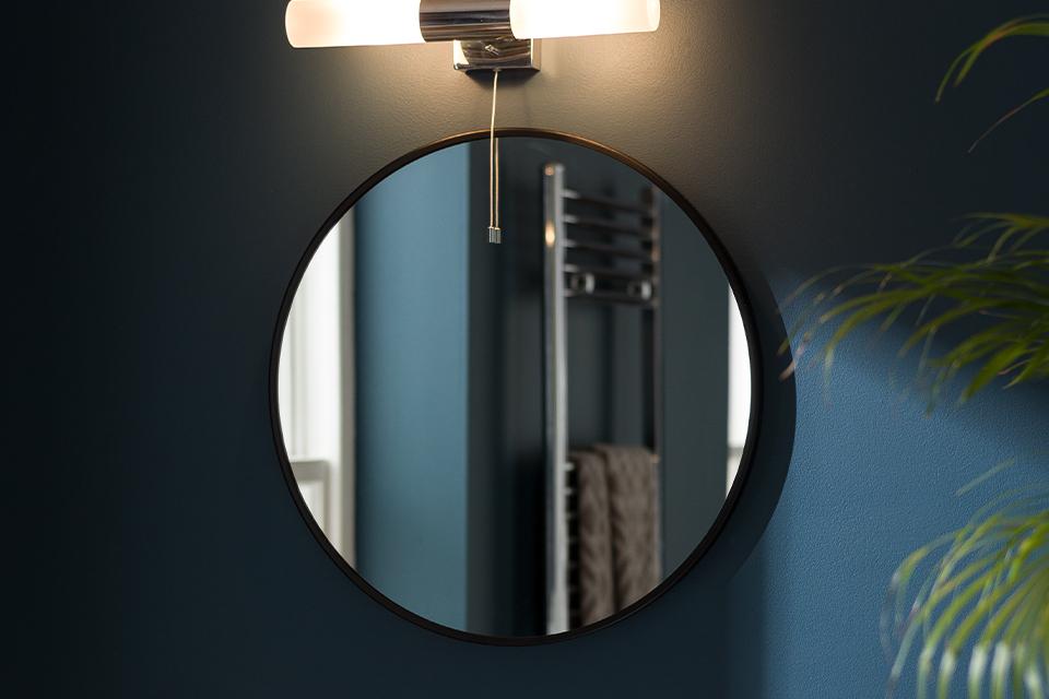 Image of a round, black mirror with a bar light above it.