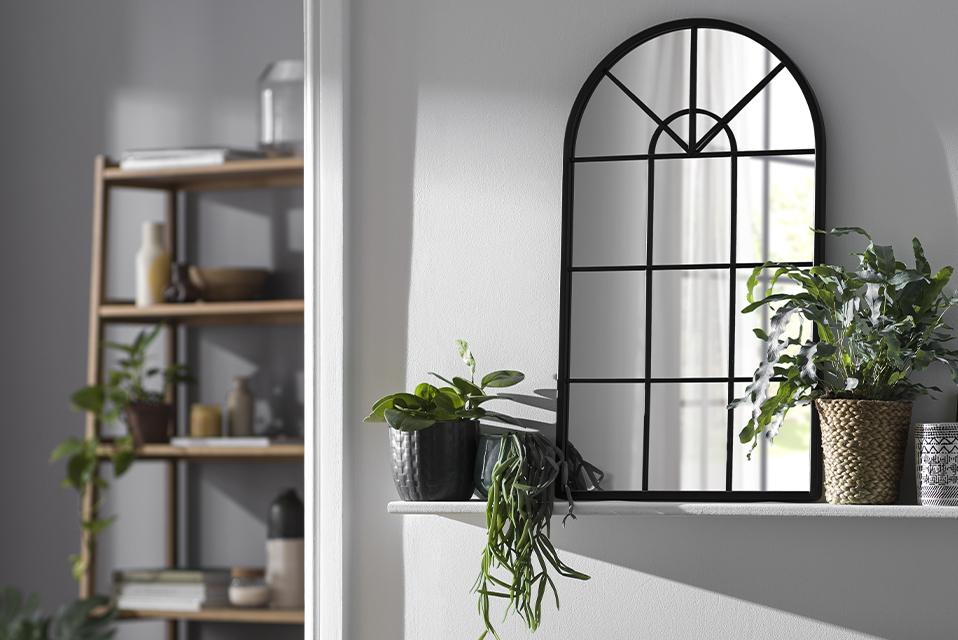 A window pane mirror on a floating shelf above a green velvet sofa.