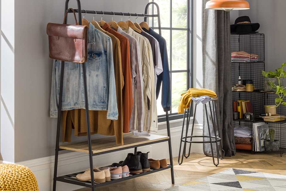 Black clothes rail with wooden slatted shelf on bottom filled with clothes.