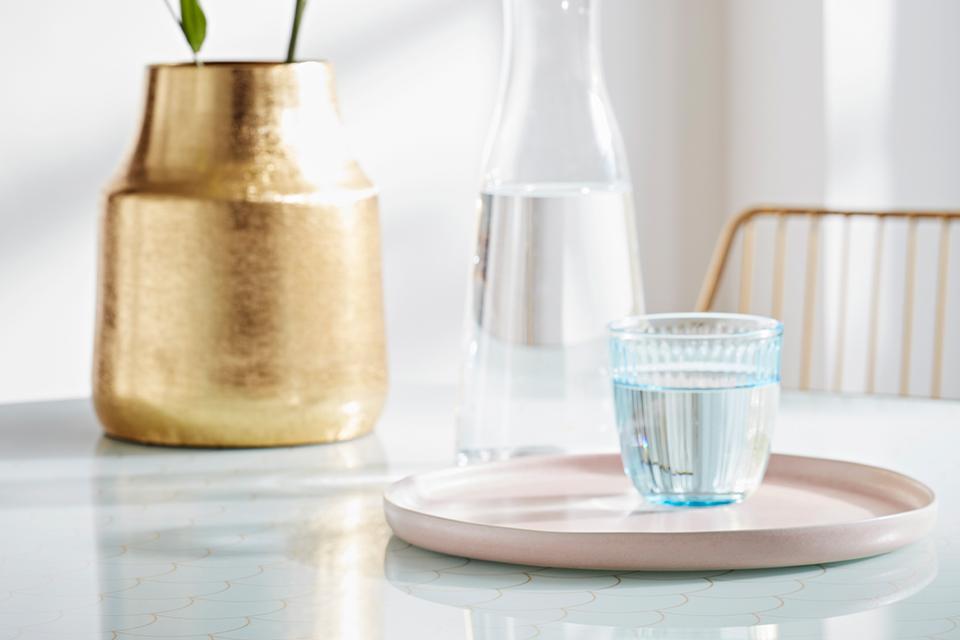 A textured glass tumbler on a pale pink serving tray with a brushed gold plant pot in the background.