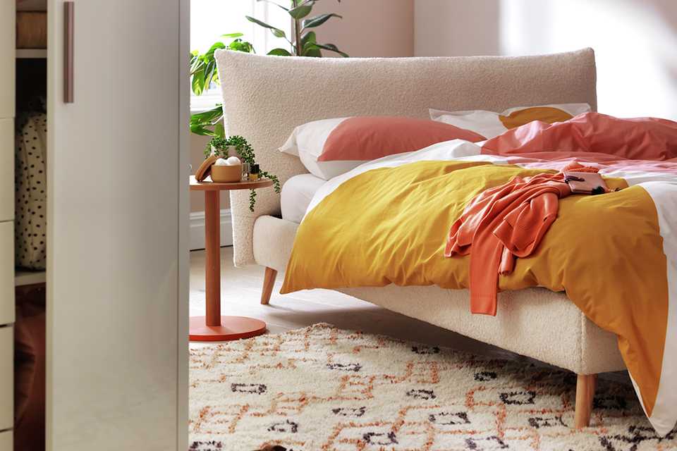 Cream upholstered boucle bed with yellow and white bedding.