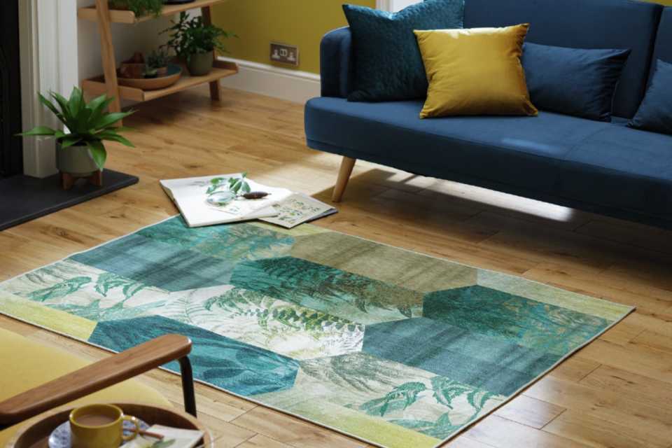A blue-green patchwork rug on a wooden floor beside a navy blue sofa.