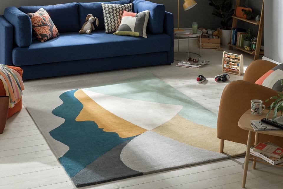 An abstract pastel coloured rug on a white wooden floor beside a navy blue sofa.