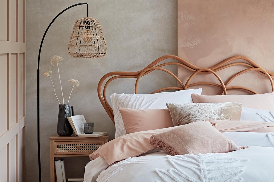 Bedroom with a rattan bedframe and floor lamp with white and pink bedding.