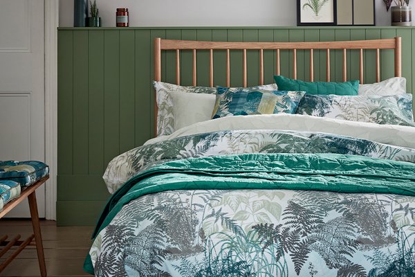 Green and white botanical print bedding on a wooden frame bed.