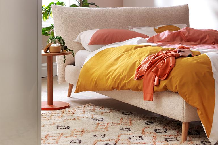 Image of a bedroom with a geomtric rug on the floor and a bed with a red and pastel duvet cover.