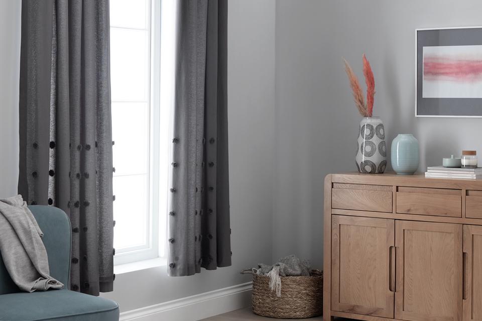Bedroom with grey bobble curtains and oak chest of drawers.