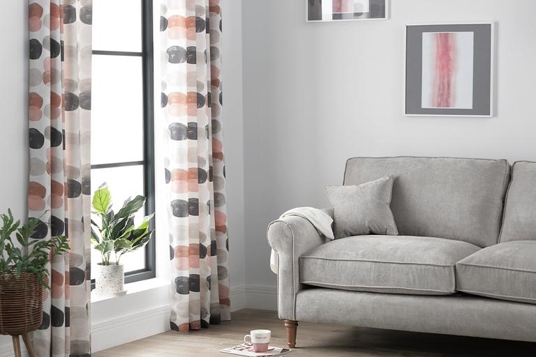 Living room with grey velvet sofa and patterned grey and pink curtains.