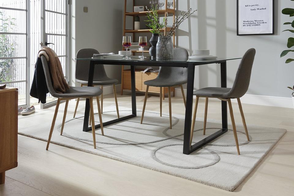 A glass-topped dining table with black legs and grey upholstered chairs.
