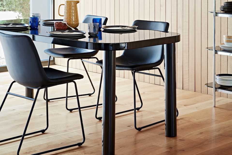 A black dining table with a glass top and rounded corners with black mid-century style chairs.