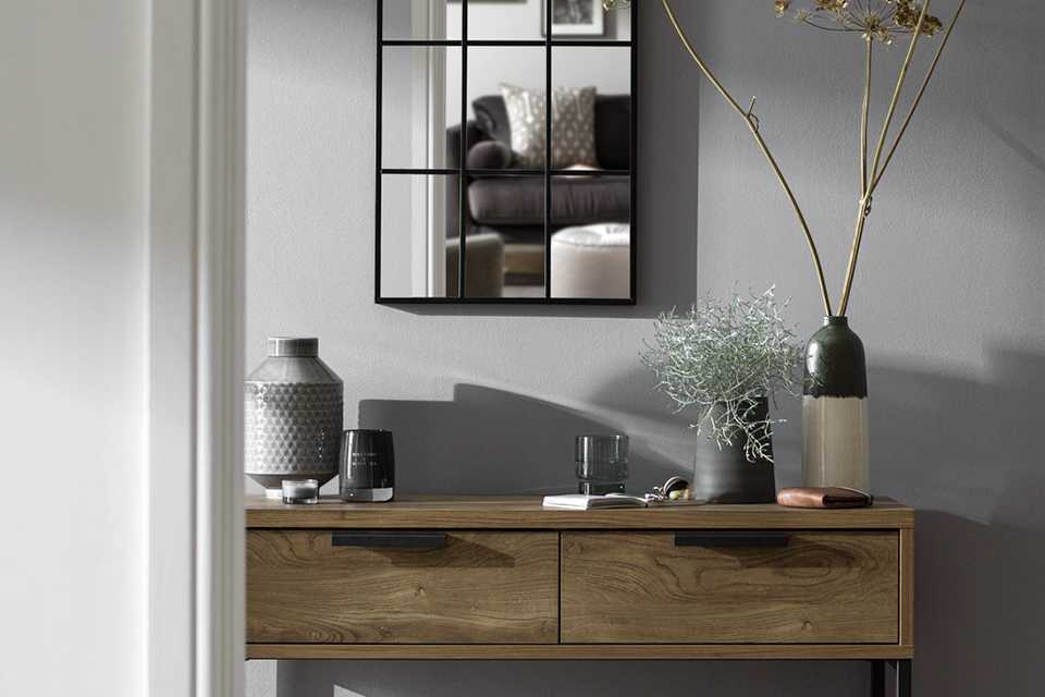 A grey hallway with a slim walnut side table decorated with modern, minimalist vases.