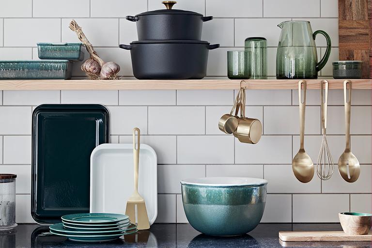 Kitchen top and shelf with utensils and tableware in green and brass.