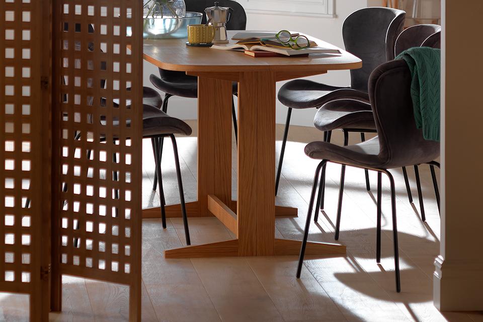 Dining room with wooden table, grey velvet chairs and a room dividing wooden screen.