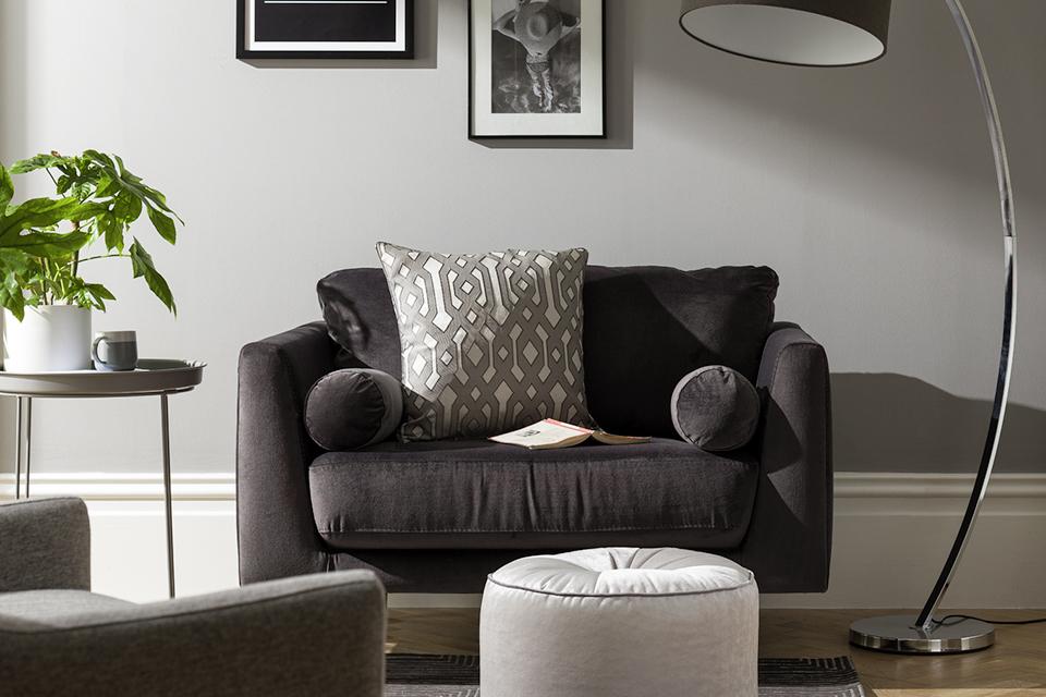 A black fabric loveseat beside a tall, arched floor lamp in pale grey living room.