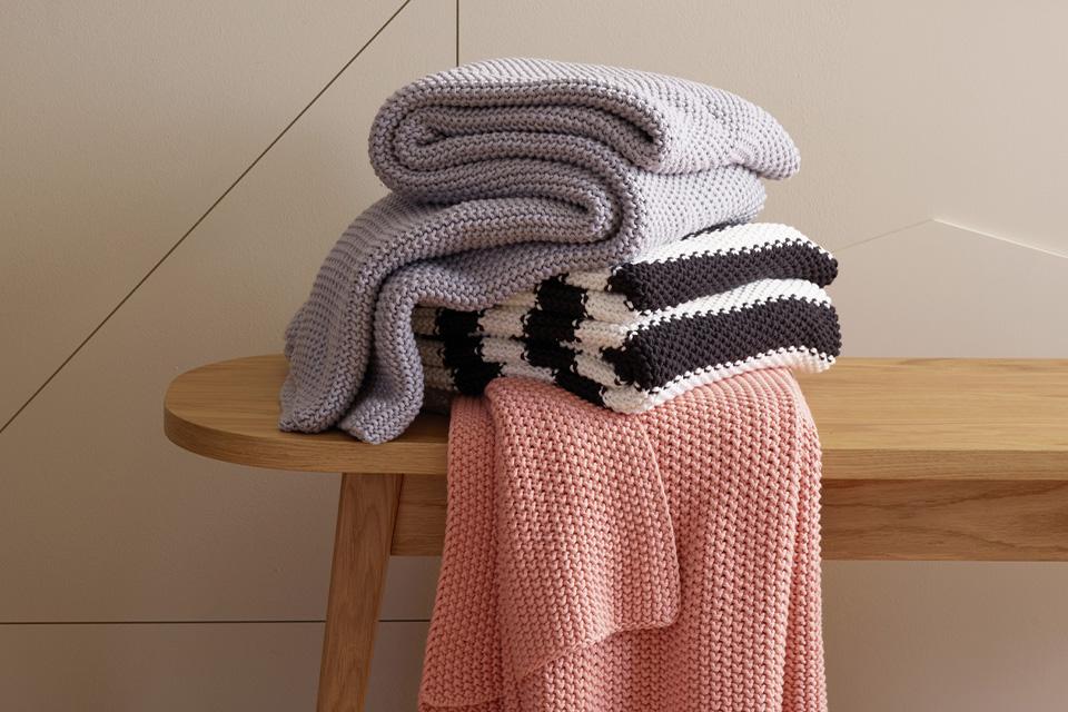 A folded pile of throws on a wooden bench.