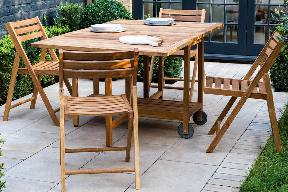 An image of a wooden table and chair set on a patio with surrounding flower beds.
