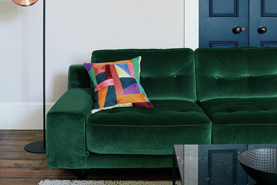 Image of a green velvet sofa with multicoloured cushion in living room.