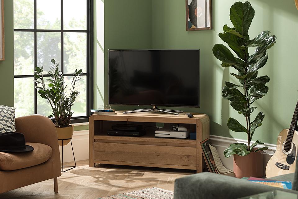Image of a wooden corner TV stand in a green living room.