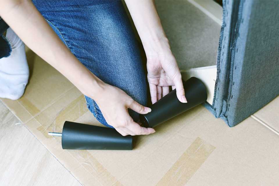 A woman attaching a plastic leg to a sofa.