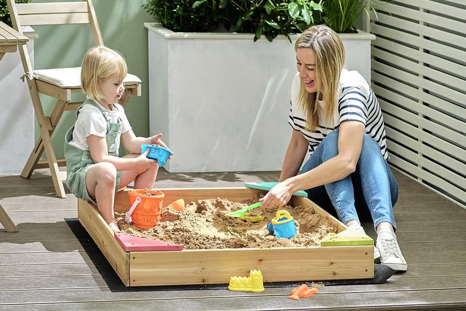 Mum and child playing outside in a wooden sand box
