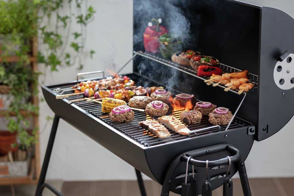 An Argos Home Drum Charcoal BBQ with sizzling food on it.