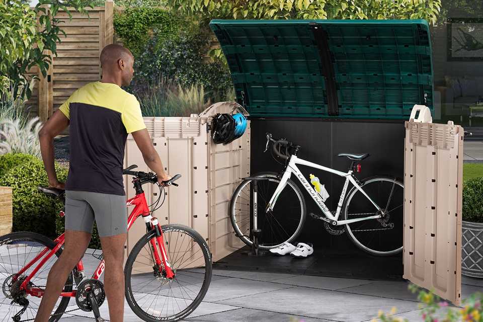 A man storing his bike in a Keter Store It Out Ultra 2000L Garden Bike Shed in beige in green.