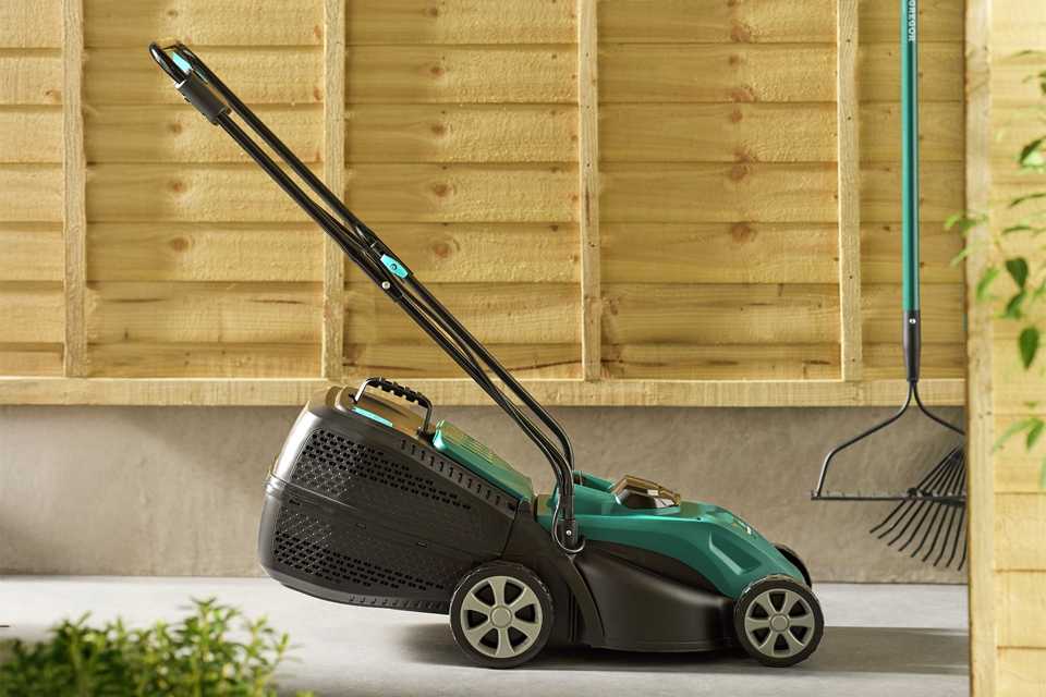 A green McGregor lawnmower displayed against a wooden backdrop.