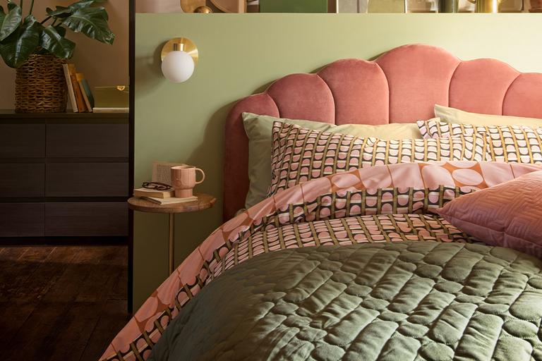 A pink velvet bed in a green bedroom with brass accessories.