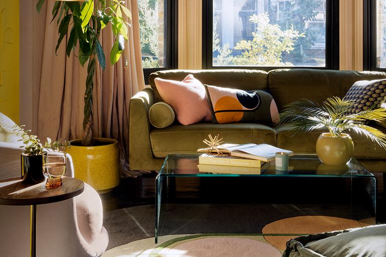 A yellow living room with green sofa, pink curtains and a glass coffee table with other home accessories.