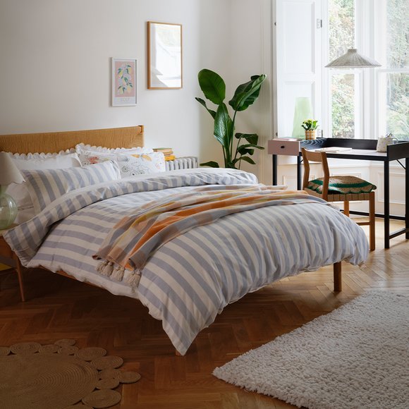 A bed with blue and white striped print on the bedding in a white bedroom.