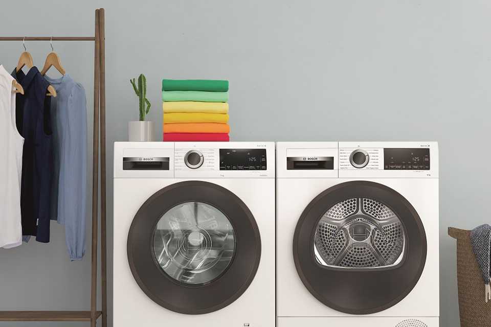 A white Bosch washing machine and a heat pump tumble dryer next to some clothes on a rack.