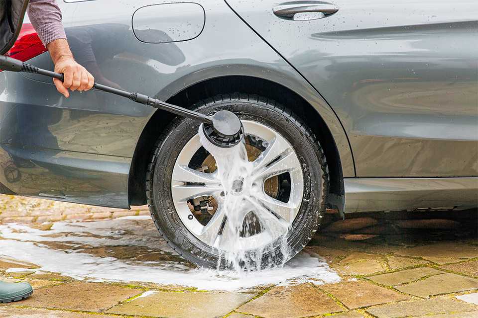 A man using brush attachment of 2000W Spear & Jackson pressure washer on a car tyre.