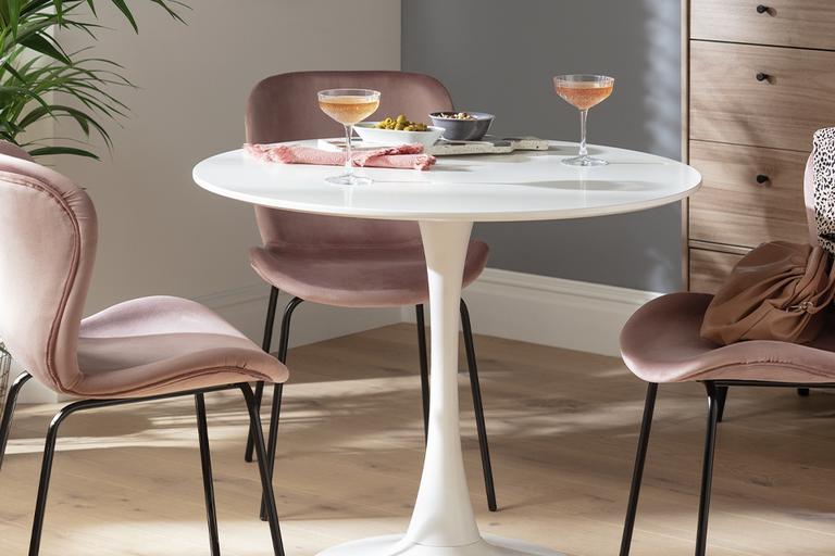 Image of three pale pink, velvet chairs around a round, white table with cocktail glasses on top.