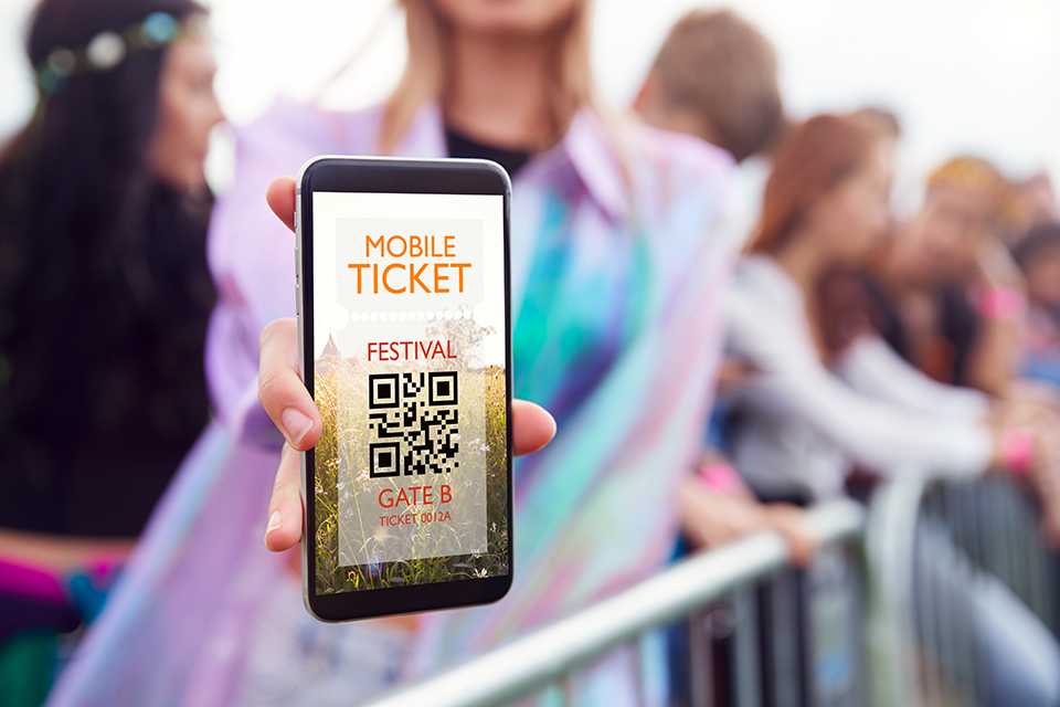 A girl in a pink raincoat showing her festival ticket barcode on her phone.
