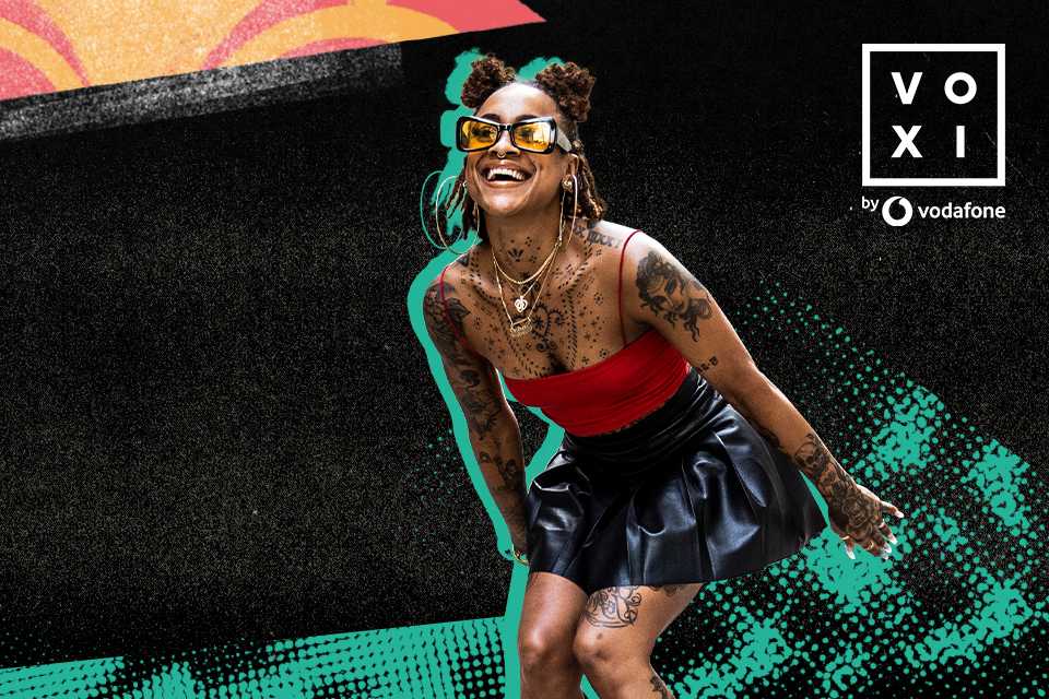 A girl with tattoos, yellow glasses and funky jewllery dancing.